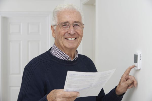 Smiling Senior Man With Bill Adjusting Central Heating Thermostat