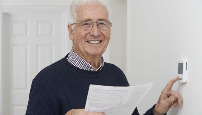 Smiling Senior Man With Bill Adjusting Central Heating Thermostat