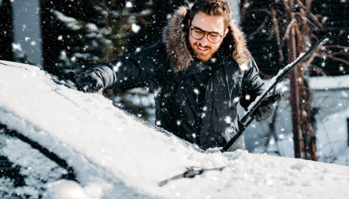 portrait of smiling man cleaning snow off his car during winter snowfall