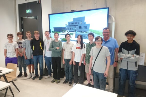 Der InnovationSPIN, gebaut in Minecraft, auf dem Bildschirm mit dem stolzen Team des Minecraft Bauprojekts., zweiter von rechts: Thomas Mahlmann (zdi-Zentrum Lippe.MINT), fünfter von links: Fabrice Magdanz (Kursleitung) mit den Schülerinnen und Schülern.