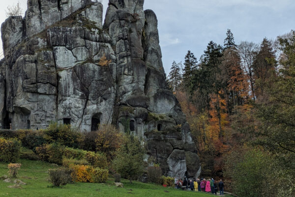 Bei herbstlicher Stimmung betrachtet eine Besuchergruppe das offene Felsengrab an den Externsteinen