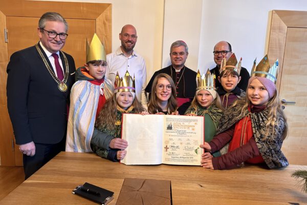 Bürgermeister Michael Dreier (ganz links) in das Goldene Buch der Stadt ein (v.l.): die Sternsingerinnen und Sternsinger Oskar, Svea, Irene, Leander, und, Emma, Domvikar Dr. Stefan Ottersbach, Erzbischof Dr. Udo Markus Bentz, Pfarrer Dirk Bingener und Helena Schmidt (sitzend), BDKJ-Diözesanseelsorgerin.