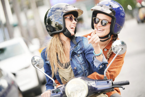 Happy young women riding scooter together in city